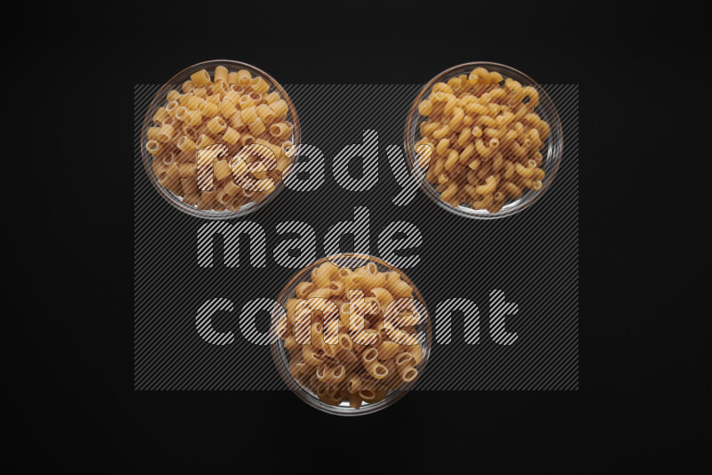 Different pasta types in glass bowls on black background