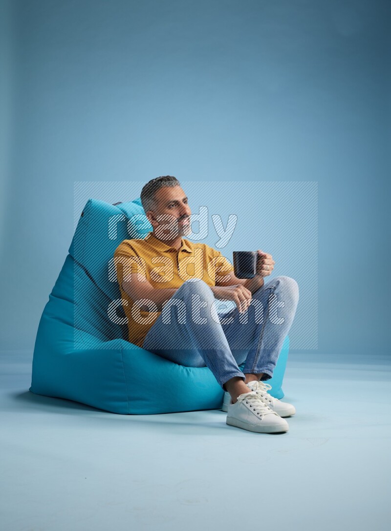 A man sitting on a blue beanbag and drinking coffee