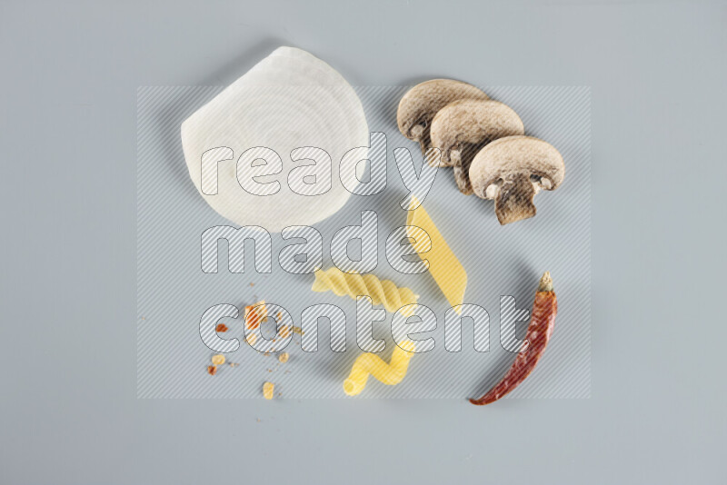 Raw pasta with different ingredients such as cherry tomatoes, garlic, onions, red chilis, black pepper, white pepper, bay laurel leaves, rosemary, cardamom and mushrooms on light blue background