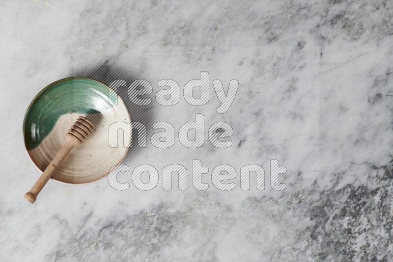 Multicolored pottery plate with wooden honey dipper in it on grey marble background