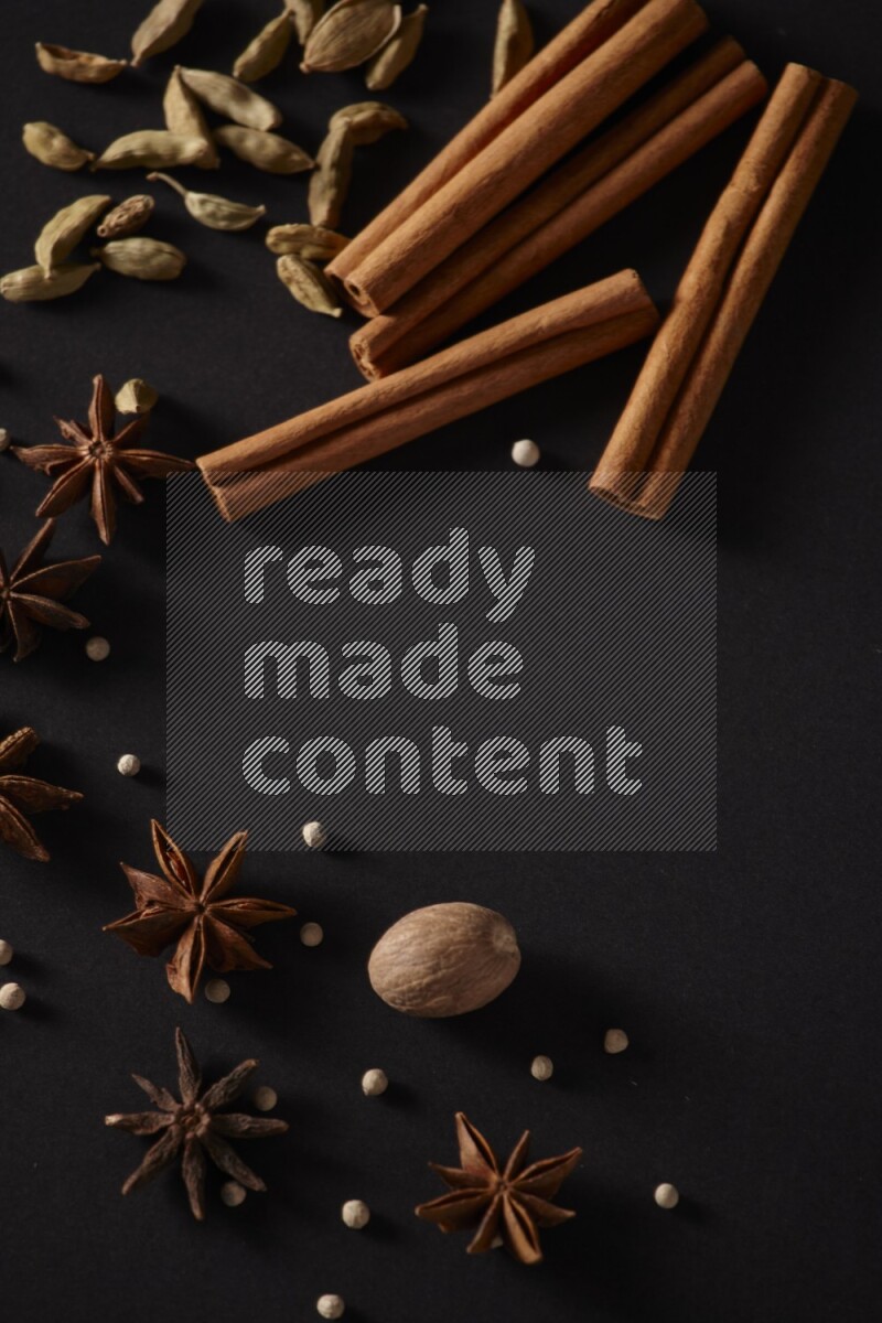 Cinnamon sticks, cardamom, star anise, nutmeg and white peppers on a black background
