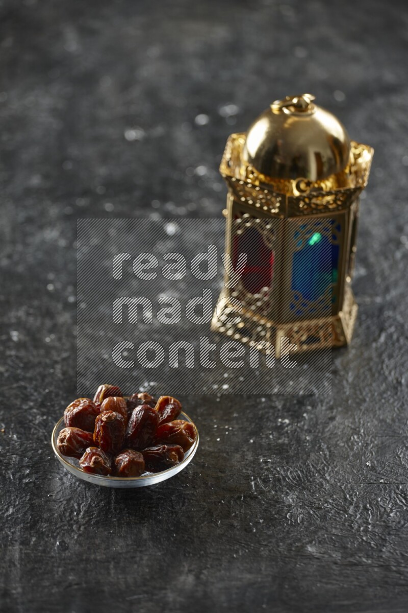 A golden lantern with different drinks, dates, nuts, prayer beads and quran on textured black background