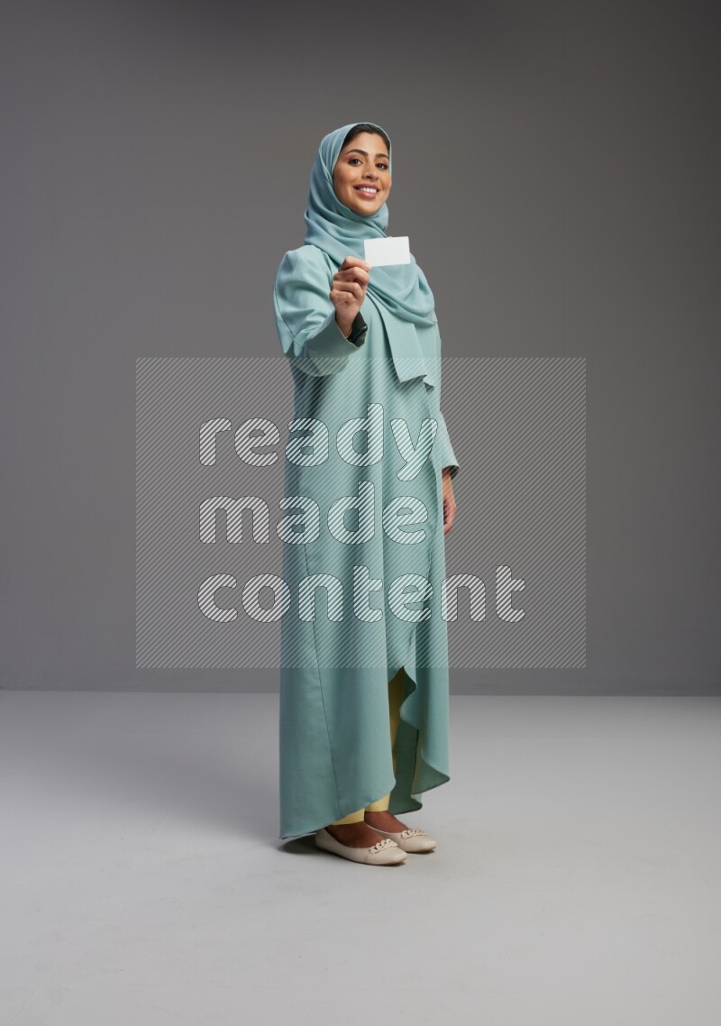 Saudi Woman wearing Abaya standing holding ATM card on Gray background