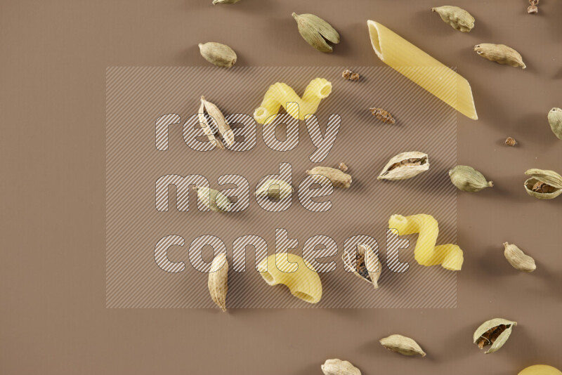 Raw pasta with different ingredients such as cherry tomatoes, garlic, onions, red chilis, black pepper, white pepper, bay laurel leaves, rosemary and cardamom on beige background