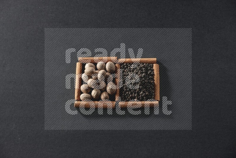 مربعان من أعواد القرفة ممتلئان بجوزة الطيب وحبوب الفلفل الأسود علي خلفية سوداء