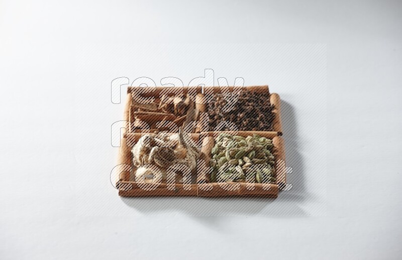 4 مربعات من أعواد القرفة ممتلئة بالهيل والقرفة والقرنفل والزنجبيل المجفف على أرضية بيضاء