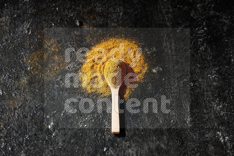 A wooden spoon full of turmeric powder on textured black background