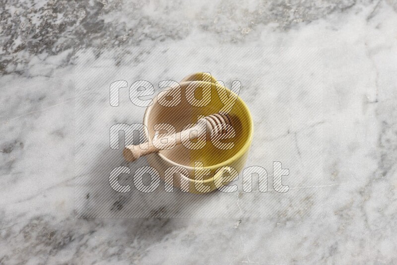 Multicolored pottery bowl with wooden honey dipper in it on grey marble background