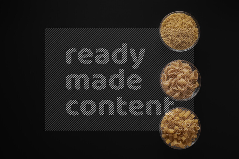 Different pasta types in 3 glass bowls on black background