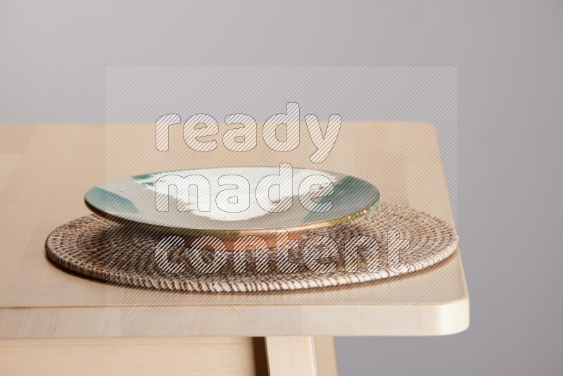 multi-colored pottery Plate placed on a big light colored straw placemat on the edge of wooden table
