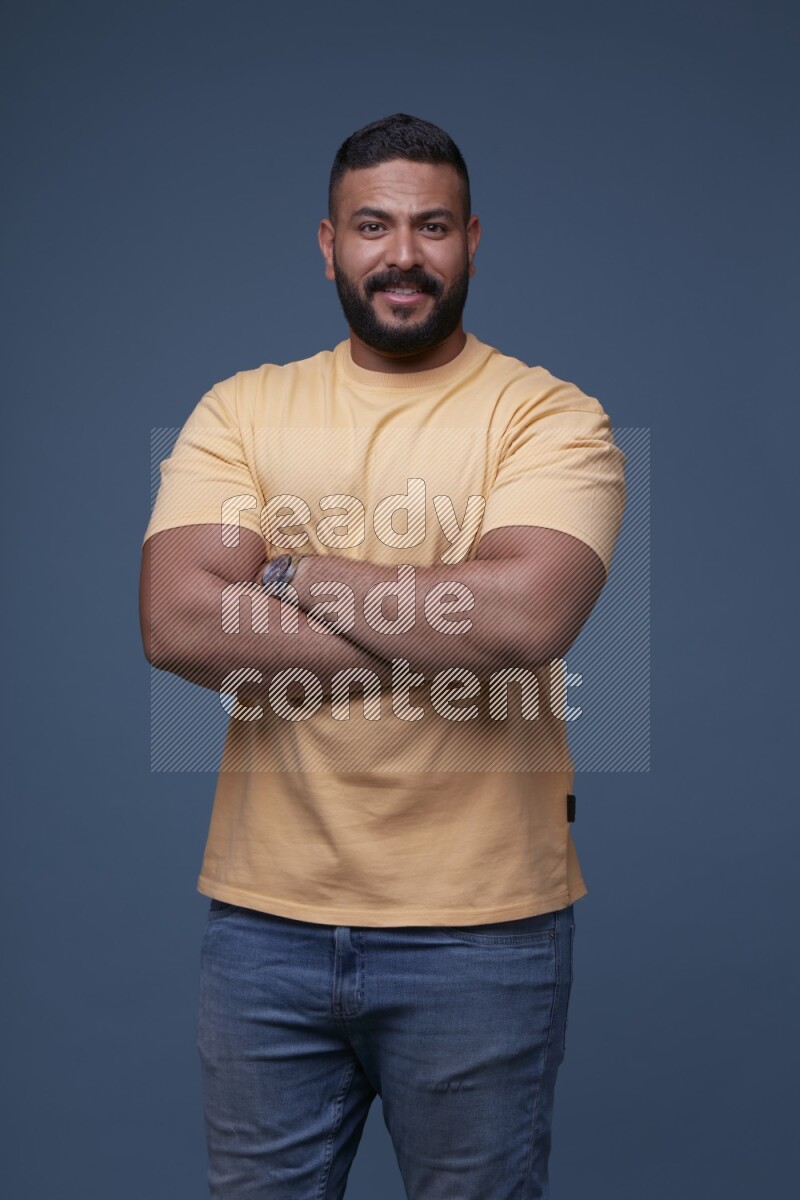 A man posing in a blue background wearing a yellow shirt