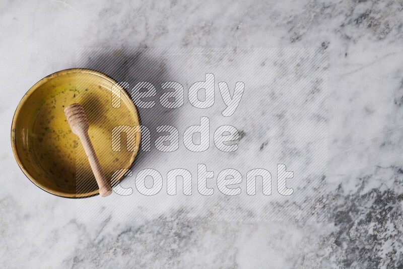 وعاء فرن فخاري متعدد الألوان مع ملعقة عسل خشبية بداخله على خلفية من الرخام الرمادي