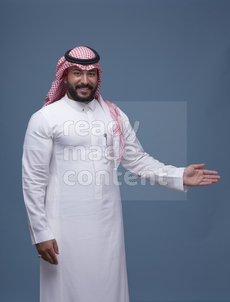 A man pointing on blue background wearing Saudi Thob with Shomag