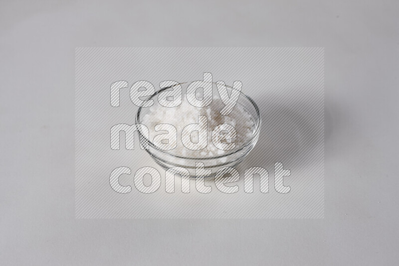 A glass bowl full of coarse sea salt crystals on white background