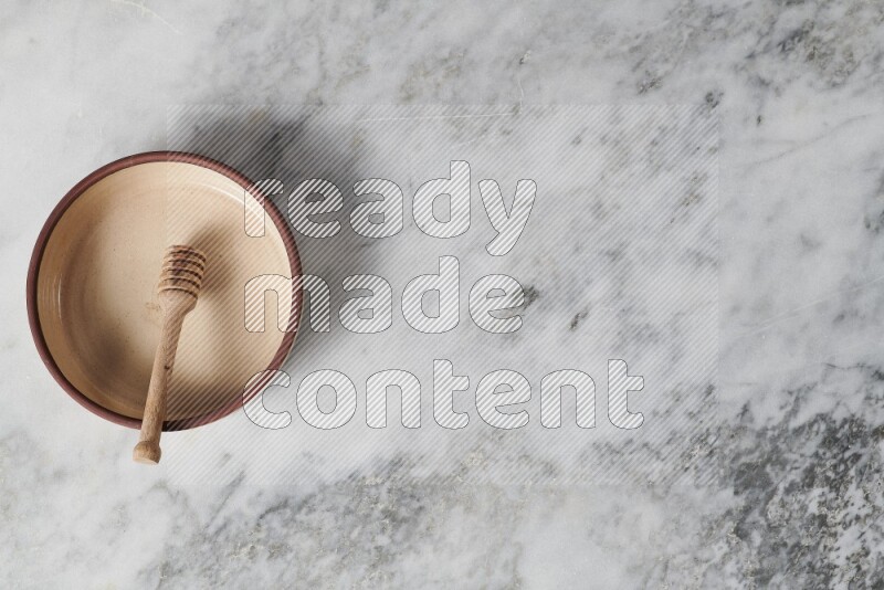 Beige pottery oven plate with wooden honey dipper in it on grey marble background