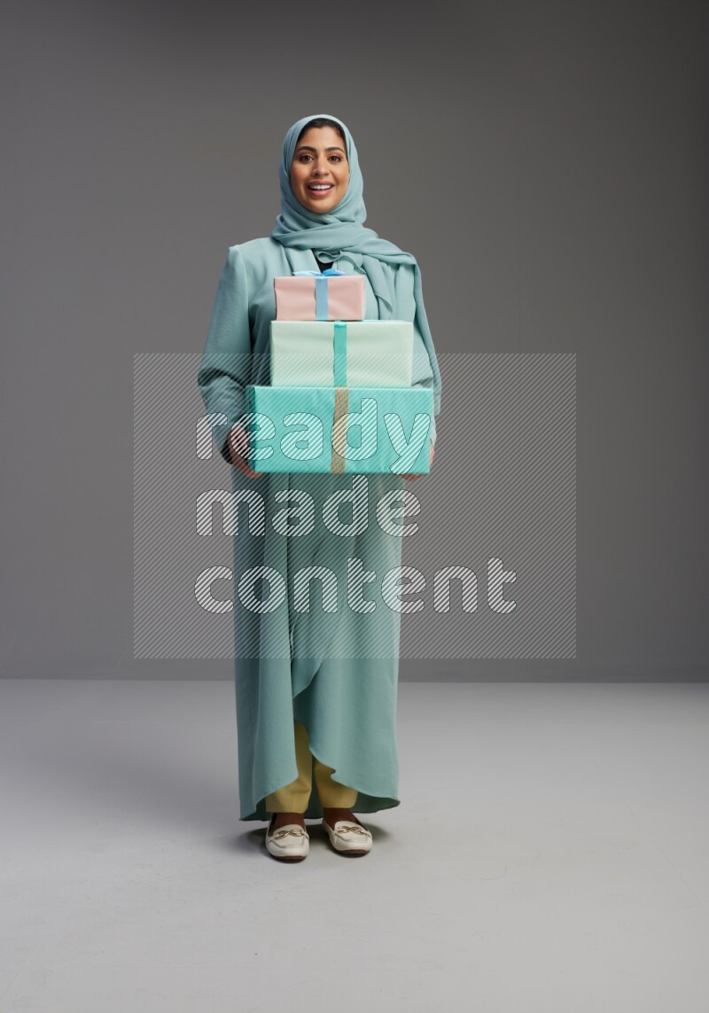 Saudi Woman wearing Abaya standing holding gift box on Gray background