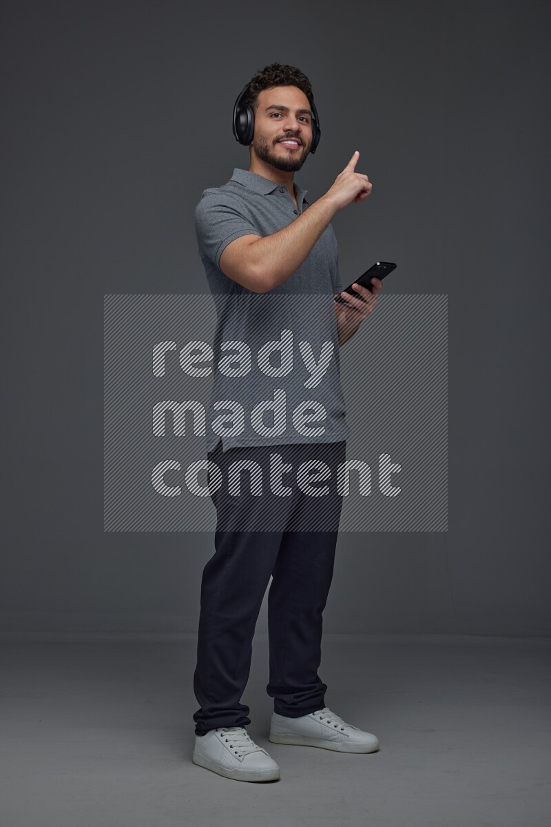 A man wearing casual and using his phone and headphone eye level on a gray background