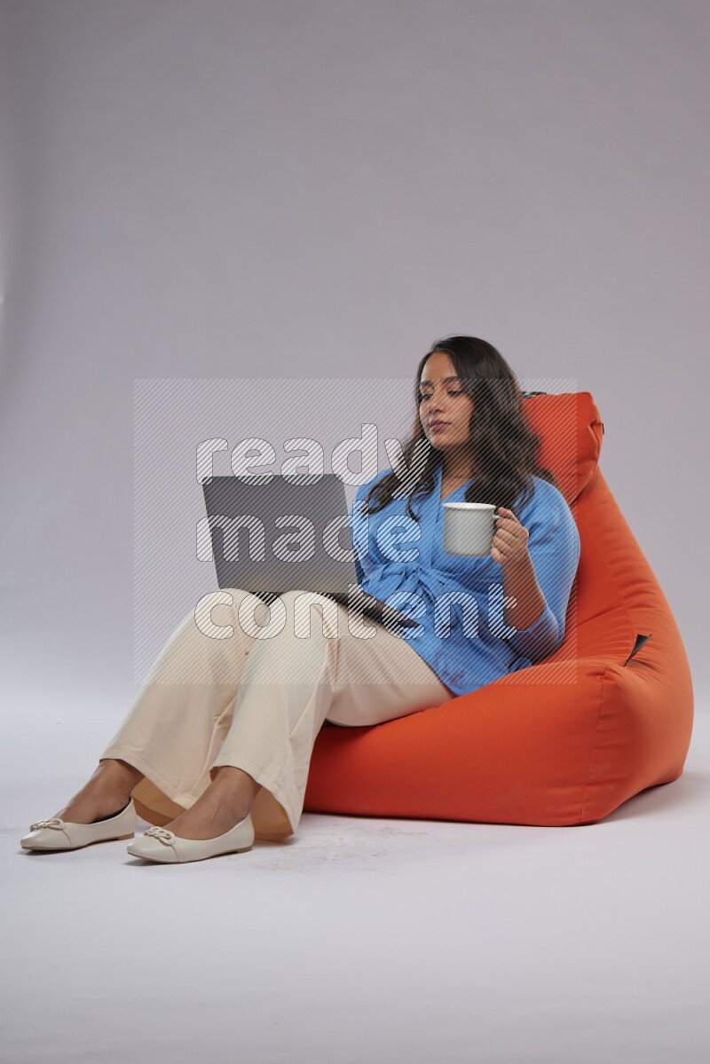 A woman sitting on an orange beanbag and working on laptop