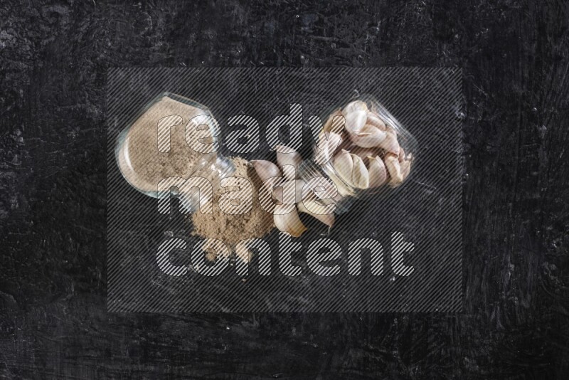 وعاءان للبهارات من الزجاج احدهما ممتلئ ببودرة الثوم والأخر ممتلئ بفصوص الثوم وكلاهما مقلوب علي خلفية سوداء