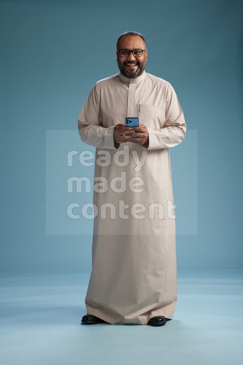 Saudi Man without shimag Standing texting on phone on blue background