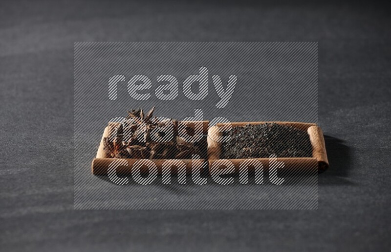 2 squares of cinnamon sticks full of star anise and black tea on black flooring