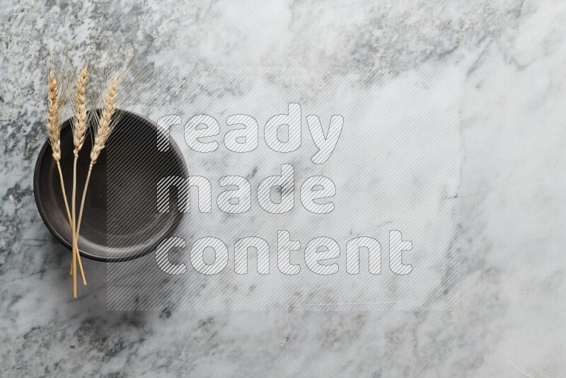 Wheat stalks on black pottery oven plate on grey marble background