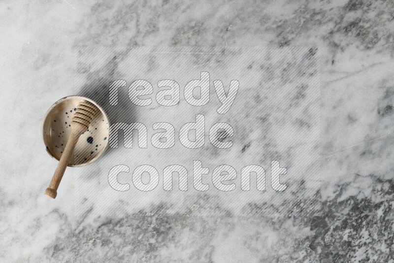 Multicolored pottery bowl with wooden honey dipper in it on grey marble background
