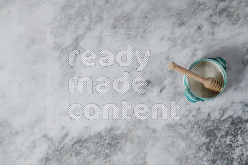 Multicolored pottery bowl with wooden honey dipper in it on grey marble background