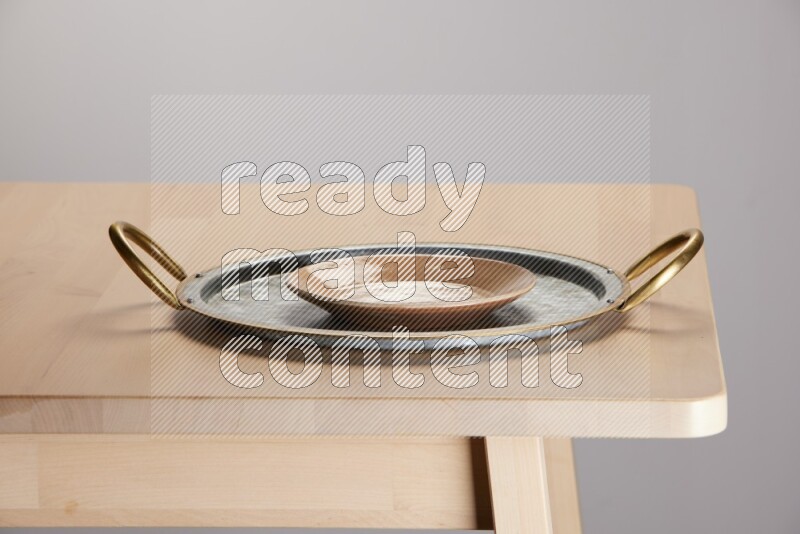 multicolored plate placed on a rounded stainless steel tray with golden handels on the edge of wooden table