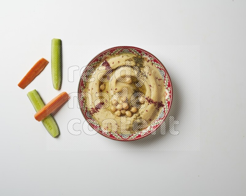 Hummus in a red plate with patterns garnished with zaatar & sumak on a white background