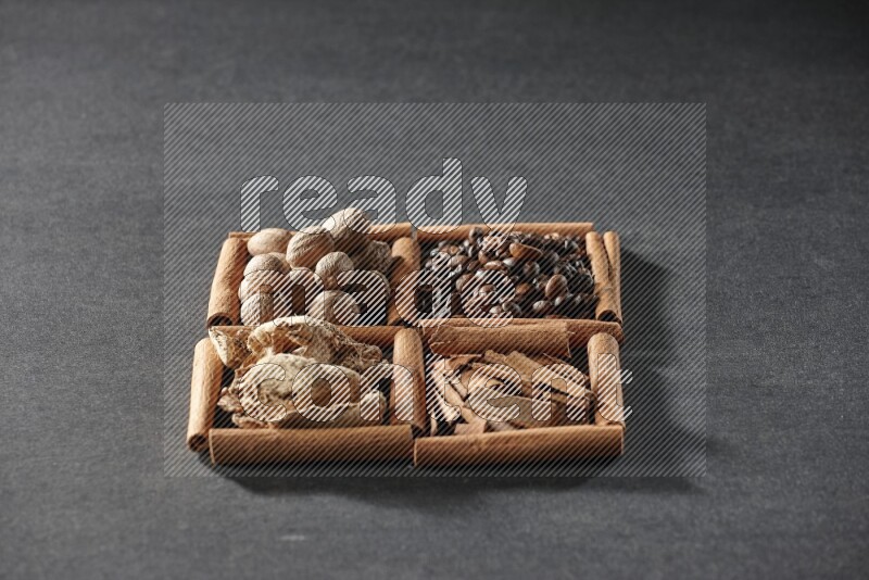 4 مربعات من عيدان القرفة ممتلئة بحبوب القهوة وقطع القرفة والزجبيل المجفف وجوزة الطيب على أرضية سوداء