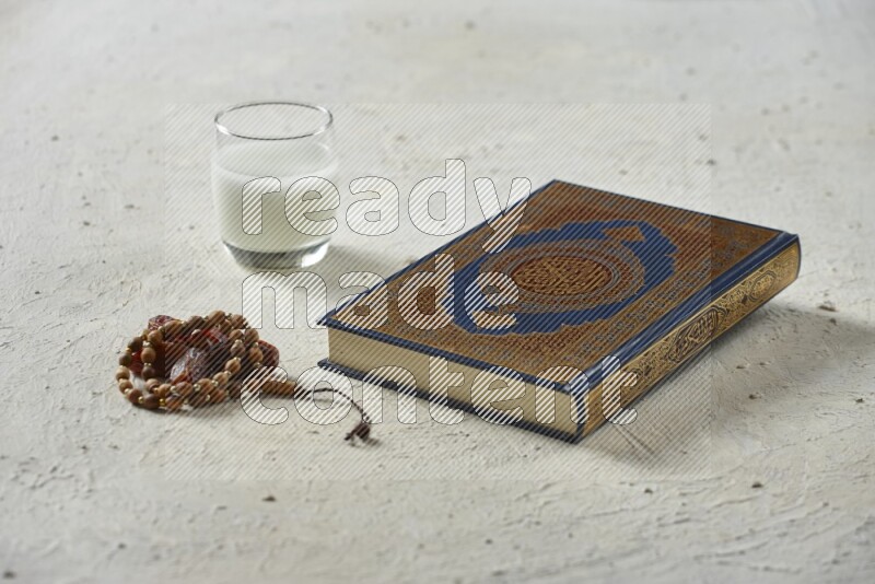Quran with dates, prayer beads and different drinks all placed on textured white background