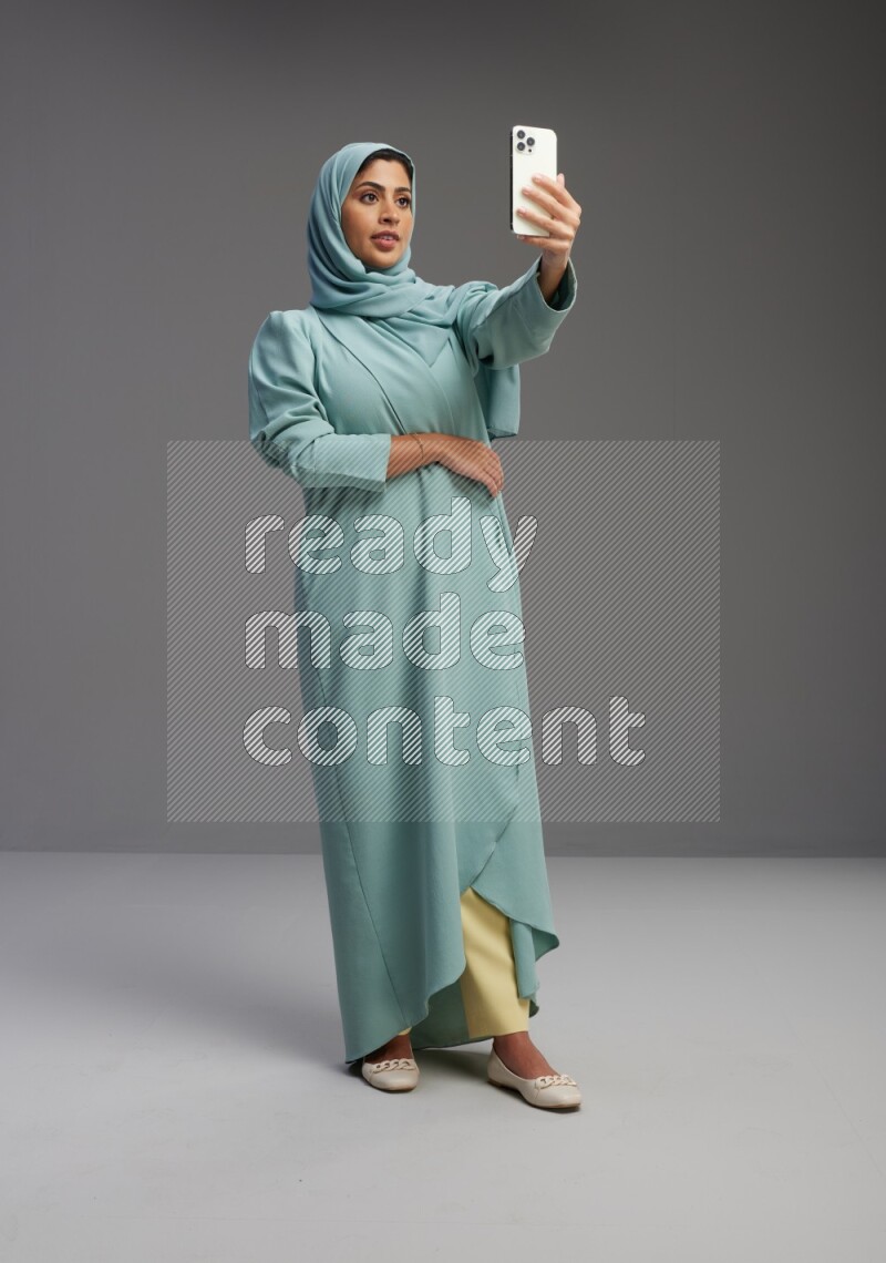 Saudi Woman wearing Abaya standing taking selfie on Gray background