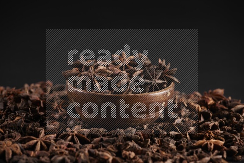 Star Anise in a wooden bowl and surrounded by more anise filling the frame on black flooring