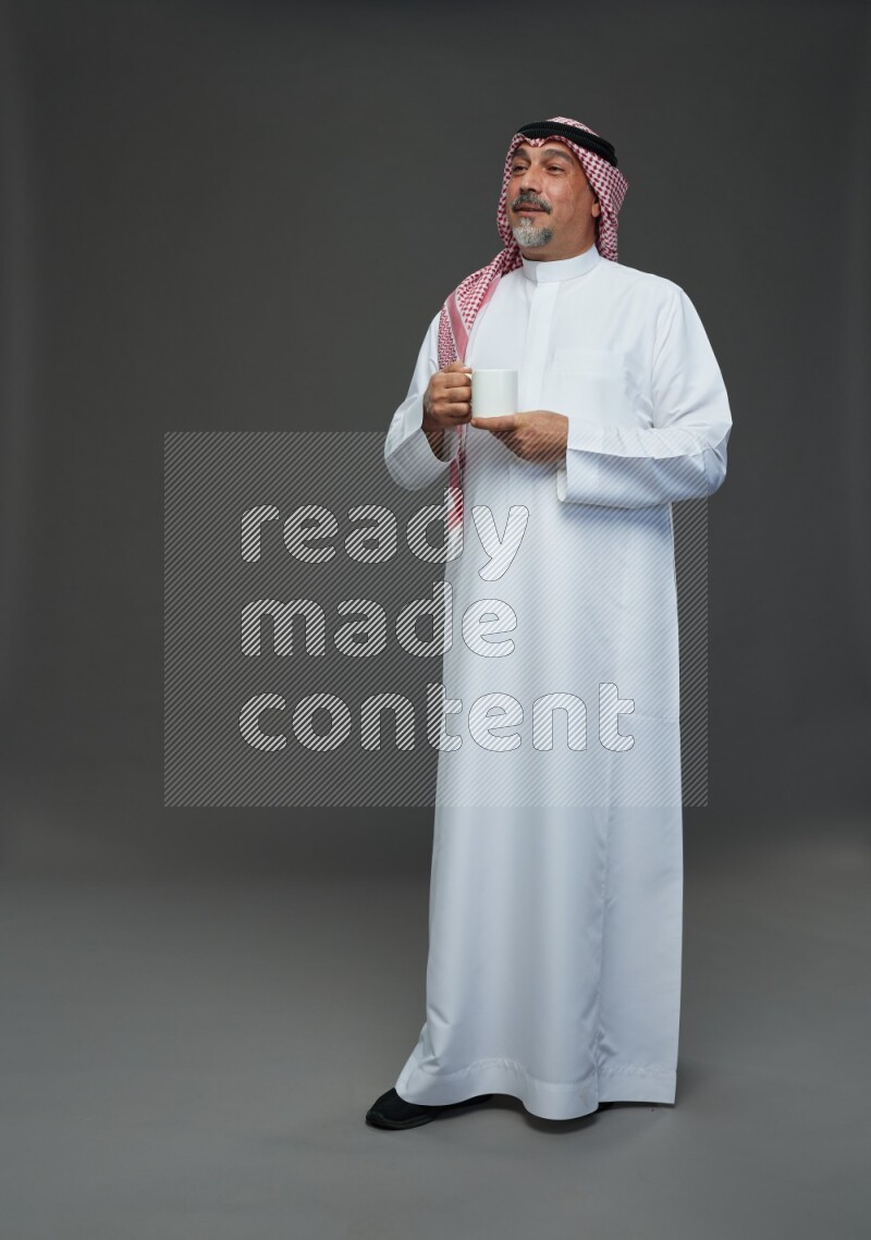 Saudi man with shomag Standing holding mug on gray background
