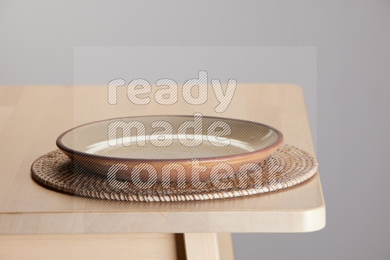 multi-colored pottery Plate placed on a big light colored straw placemat on the edge of wooden table