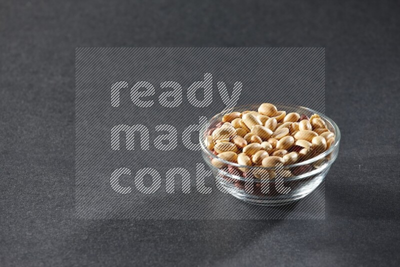 A glass bowl full of peeled peanuts on a black background in different angles