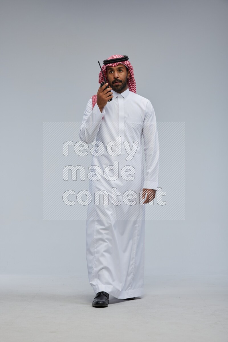 Saudi man Wearing Thob and shomag standing holding walkie-talkie on Gray background