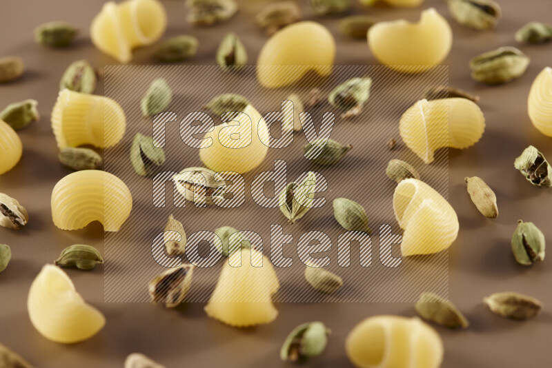 Raw pasta with different ingredients such as cherry tomatoes, garlic, onions, red chilis, black pepper, white pepper, bay laurel leaves, rosemary and cardamom on beige background