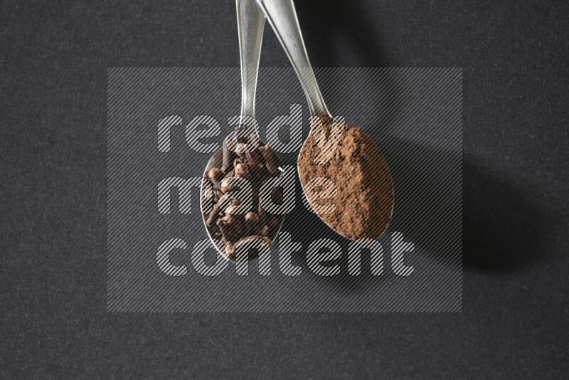 ملعقتان معدنيتان، إحداهما ممتلئة بحبوب القرنفل والأخرى ببودرة القرنفل، على خلفية سوداء