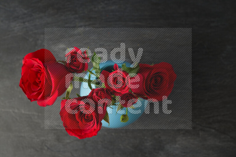 An arrangement of vivid red roses in a blue vase on black marble background