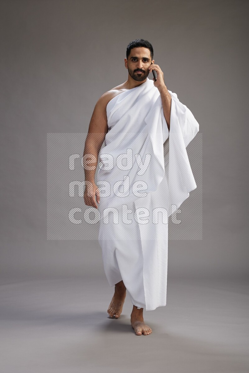 A man wearing Ehram Standing talking on phone on gray background