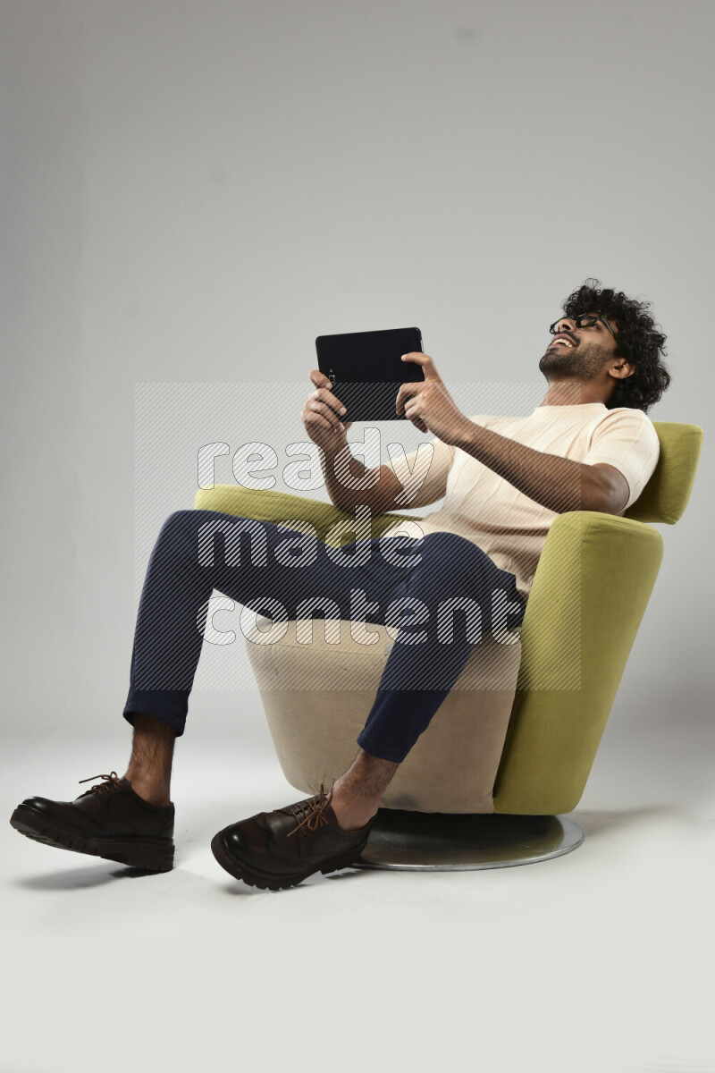 A man wearing casual sitting on a chair gaming on a tablet on white background