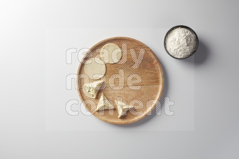 two closed sambosas and one open sambosa filled with cheese while flour aside in a wooden dish on a white background
