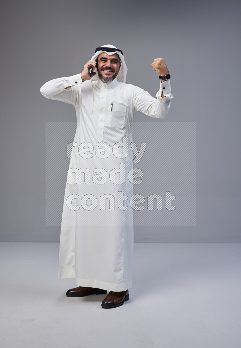 Saudi man Wearing Thob and white Shomag standing talking on phone on Gray background