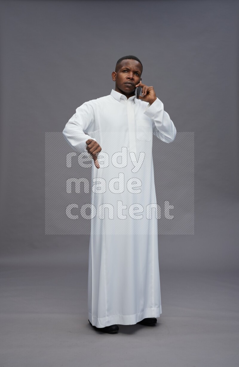 Saudi man wearing thob standing talking on phone on gray background