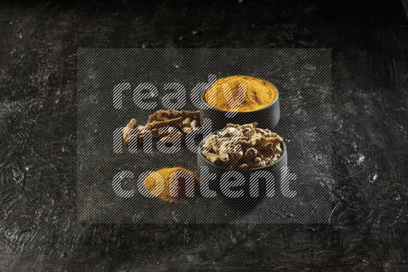 وعاءان من الفخار باللون الأسود، أحدهما ممتلئ ببودرة الكركم والآخر ممتلئ بأصابع كاملة من الكركم المجفف على خلفية سوداء