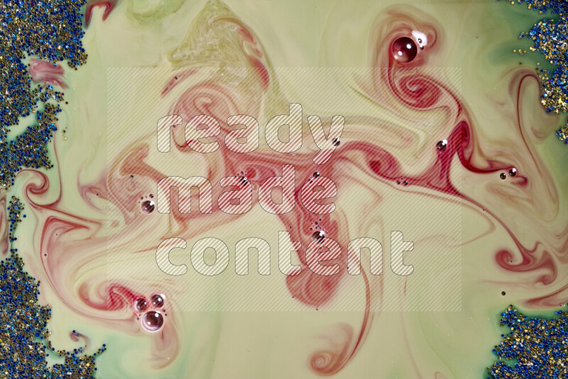 A close-up of sparkling blue and gold glitter scattered on swirling green and red background