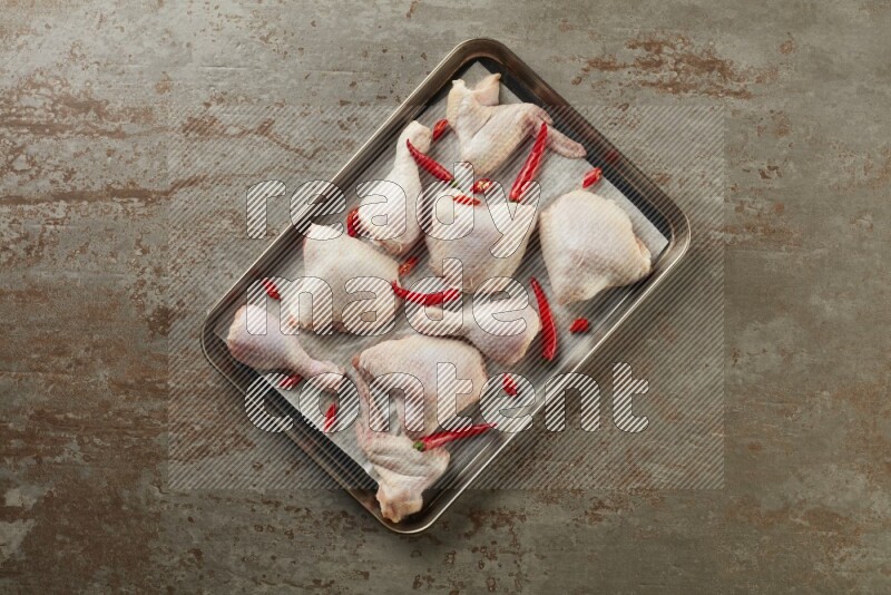 Mixed fresh chicken pieces in an oven tray on a textured rustic background