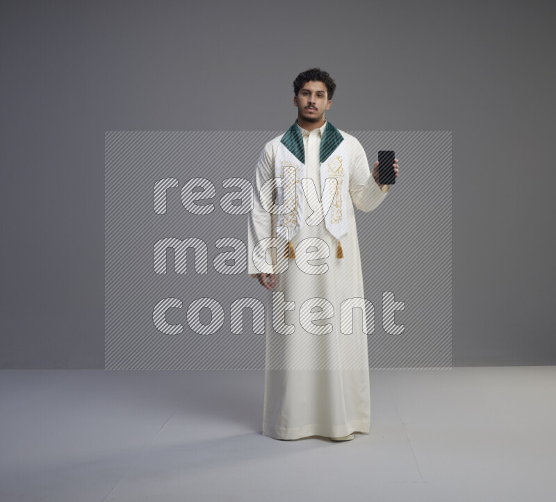 رجل سعودي يرتدي ثوب ابيض و شال يحمل جوال